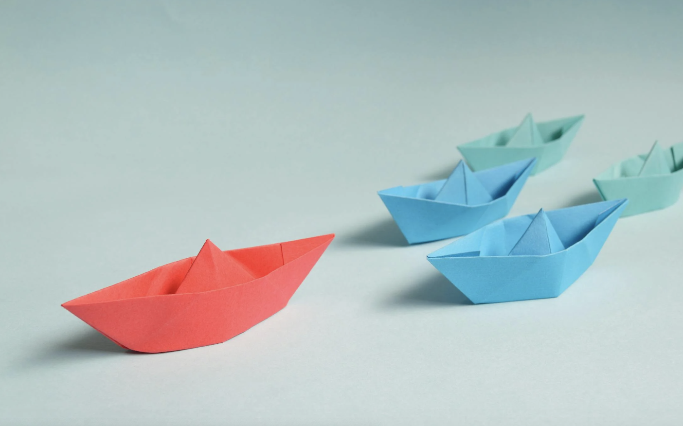 Photo of paper boats with the red boat leading the other smaller paper boats. 