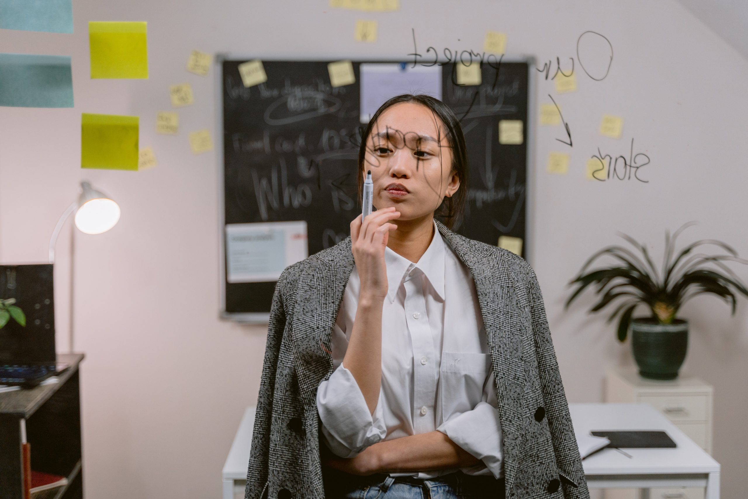 A woman in the office writing out ideas on a glass whiteboard.