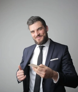 A smiling businessman in a black suit holding a card.