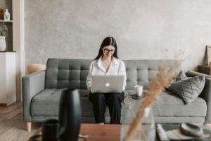 A businesswoman smiling as she sits on a couch and uses her laptop.