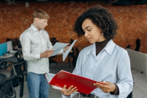 Employees Standing in White Long Sleeve Shirts Holding and Reading Paperwork Inside an Office.