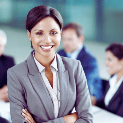 A smiling woman in a suit in front of a group of office workers.