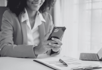 A black-and-white photo of a businesswoman smiling at her phone.