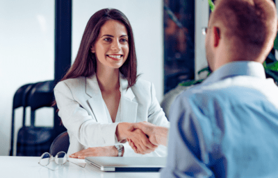 A smiling woman and a man shake hands over a table.